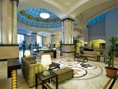 Großer Hotel-Lobby mit braunen Sesseln, Marmor-Säulen und gläserner Kuppel an der Decke.