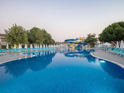 Großer, leerer Pool mit Liegestühlen und Sonnenschirmen unter klarem Himmel.