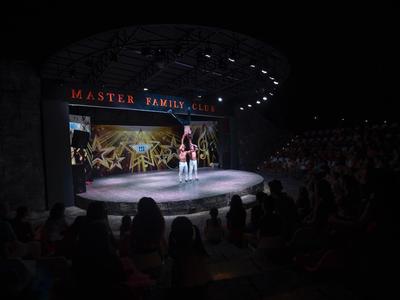 Akrobaten führen eine Show auf einer beleuchteten Bühne vor einem Publikum auf, umgeben von Dunkelheit.