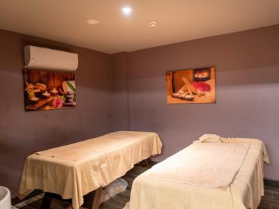 Ein ruhiger Raum mit zwei Massageliegen, weichen Decken und warmem Licht, Wände in Braun- und Beigetönen.