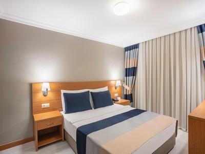 Modernes Hotelzimmer mit Doppelbett, Nachttischen, Vorhängen und Schreibtischlichtbeleuchtung.