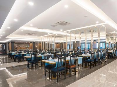 Großer, moderner Speisesaal mit blauen Stühlen, weißen Tischen und glänzendem Bodenbelag.