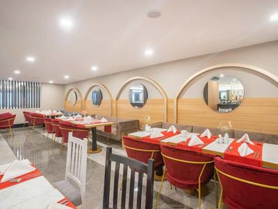 Hell beleuchteter Speisesaal mit roten und weißen gedeckten Tischen, runden Spiegeln und Holzwänden.