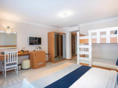 Helles Hotelzimmer mit Doppelbett, Etagenbett, Schreibtisch, TV und kleinem Kleiderschrank.