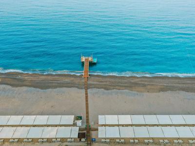 Langgezogener Steg führt über einen Sandstrand bis zum ruhigen blauen Meer.