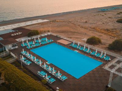 Großer rechteckiger Pool mit Liegestühlen und Sonnenschirmen am Strand.