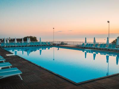 Ein ruhiger Pool mit Liegestühlen daneben bei Sonnenuntergang am Meer.