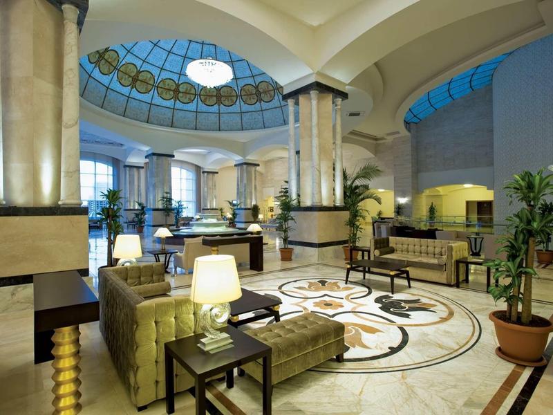 Großer Hotel-Lobby mit braunen Sesseln, Marmor-Säulen und gläserner Kuppel an der Decke.