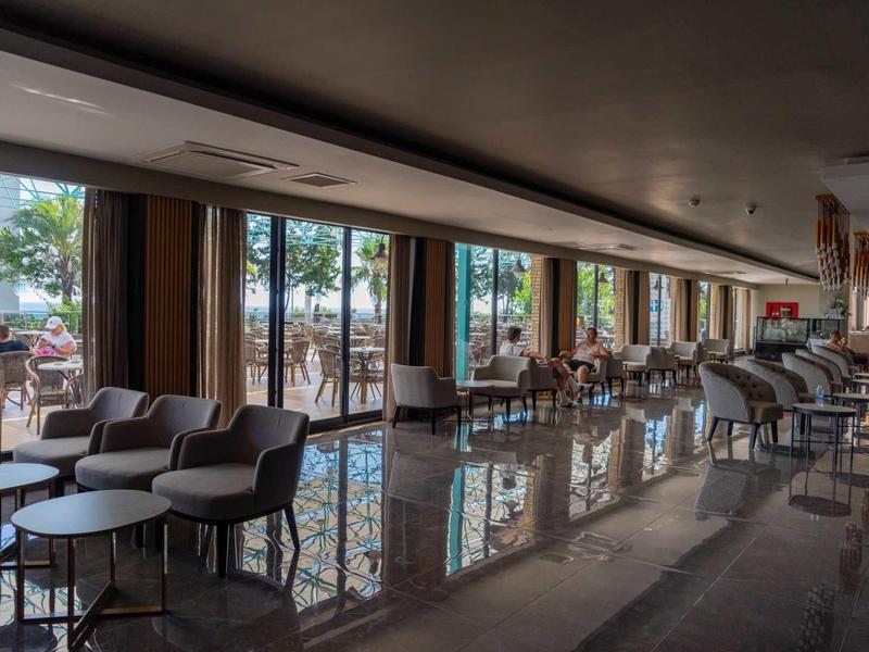 Großer, heller Speisesaal mit Glasfront und moderner Sitzgruppe aus Sesseln und Tischen.