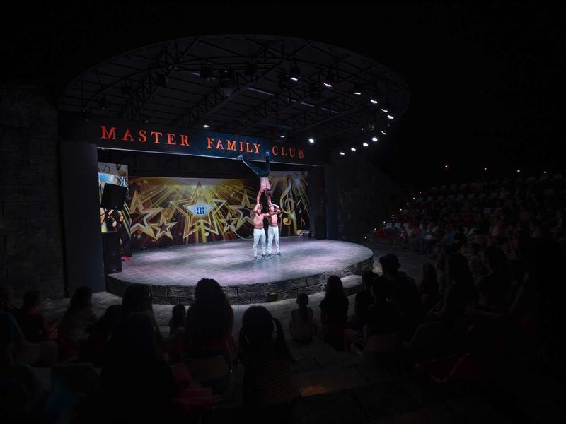 Dunkle Bühne mit Akrobaten in roter Kleidung bei einer Show, Publikum im Vordergrund.