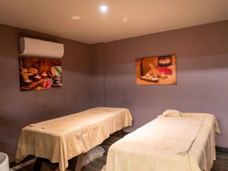 Ein ruhiger Raum mit zwei Massageliegen, weichen Decken und warmem Licht, Wände in Braun- und Beigetönen.