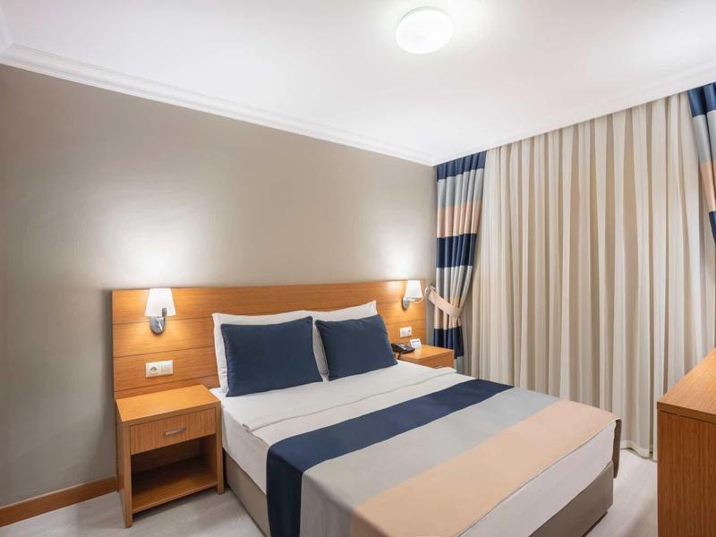 Modernes Schlafzimmer mit großem Bett, blauen und weißen Betttextilien und Vorhängen, Nachttischen und Deckenleuchte.