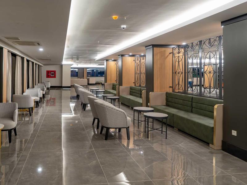 Moderner, langer Loungebereich mit beigen Stühlen, grüner Bank, grauem Boden und indirekter Deckenbeleuchtung.