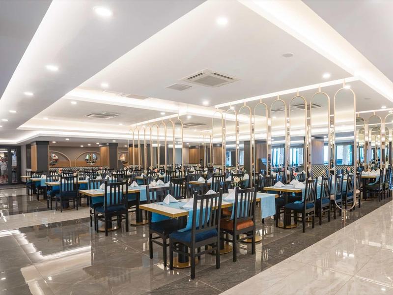 Großer, moderner Speisesaal mit blauen Stühlen, weißen Tischen und glänzendem Bodenbelag.