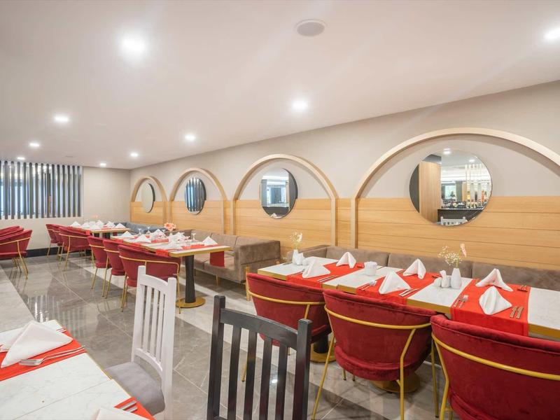 Hell beleuchteter Speisesaal mit roten und weißen gedeckten Tischen, runden Spiegeln und Holzwänden.