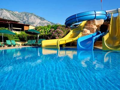 Toboggans aquatiques colorés au bord de la piscine avec montagnes en arrière-plan dans une station hôtelière.