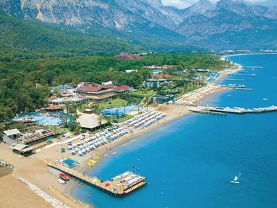 Vue aérienne d'un hôtel sur la plage avec des chaises longues, des jetées et des montagnes en arrière-plan.