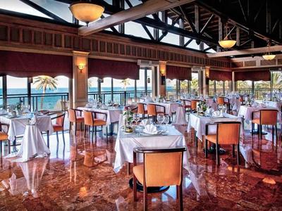 Restaurant d'hôtel lumineux avec chaises orange et vue sur la mer à travers de grandes fenêtres.