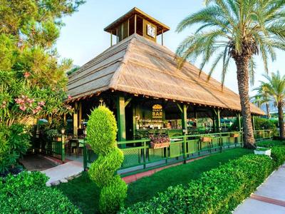 Restaurant extérieur vert avec toit de chaume et végétation tropicale dans le jardin de l'hôtel.