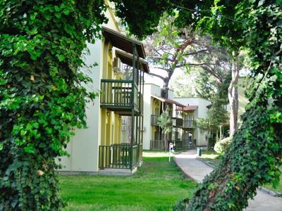 Vue sur des sentiers carrelés et des balcons d'immeubles hôteliers entourés d'arbres verts et d'herbe.