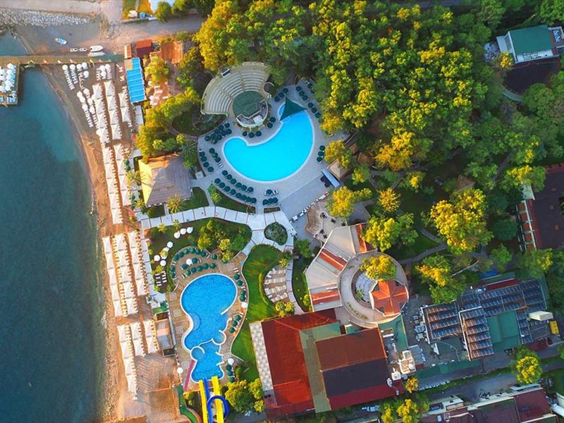 Vue aérienne d'un hôtel avec piscine, jardin et plage au bord de l'eau.
