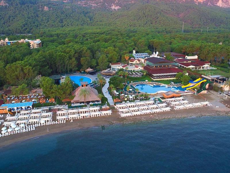 Vue aérienne d'une station balnéaire avec transats, piscines et montagnes en arrière-plan.