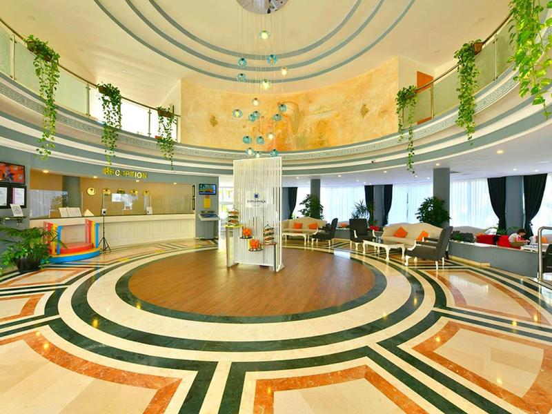 Hall d'hôtel circulaire et lumineuse avec motif de sol décoratif et verdure sur la galerie.