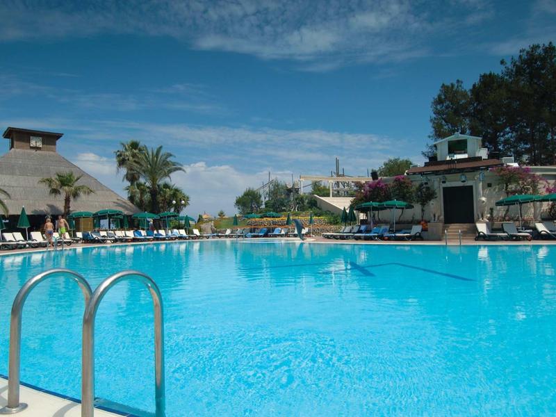 Grande piscine d'hôtel avec chaises longues et palmiers sous un ciel bleu.