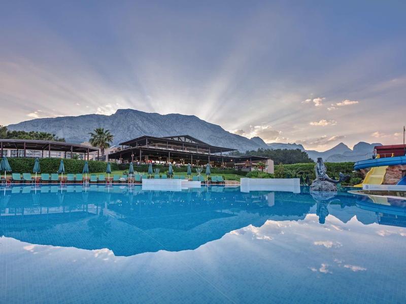 Grand piscine extérieure avec toboggans devant les montagnes au coucher du soleil.