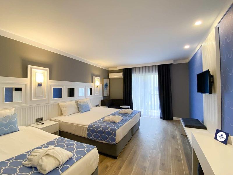 Chambre d'hôtel moderne avec deux lits, sol en bois, TV et grande fenêtre avec rideaux.