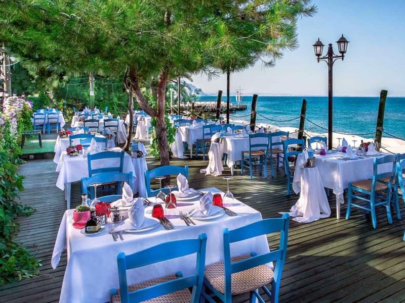 Restaurant en plein air avec chaises bleues et nappes blanches au bord de la mer.