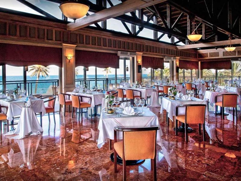 Restaurant d'hôtel lumineux avec chaises orange et vue sur la mer à travers de grandes fenêtres.