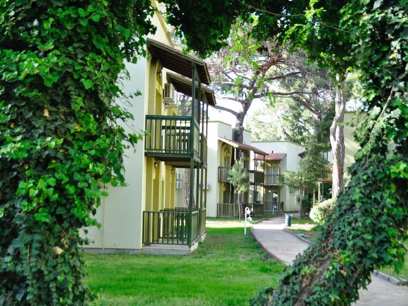 Vue sur des sentiers carrelés et des balcons d'immeubles hôteliers entourés d'arbres verts et d'herbe.