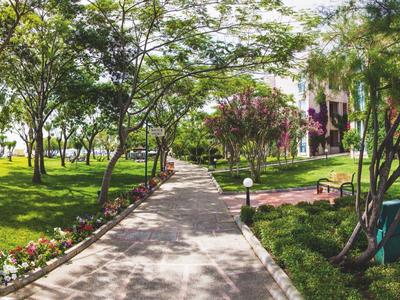 Ein gepflasterter Weg führt durch eine grüne Gartenanlage mit Bäumen und Gebäuden im Hintergrund.