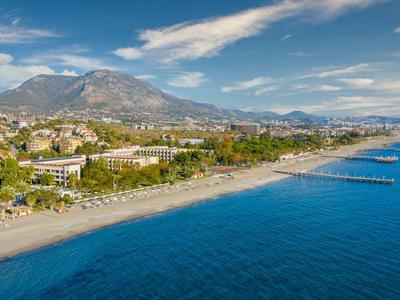Luftaufnahme eines Küstenortes mit Strand, blauem Meer und Bergen im Hintergrund.