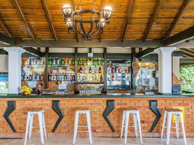 Helle Bar mit Holzdecke, Backsteinfront und weißen Barhockern unter einem Kronleuchter.