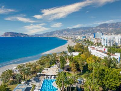Strand mit blauem Wasser, Hotels und einer großen Poolanlage in einer Küstenstadt.