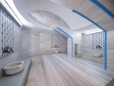 Heller, moderner Hammam mit Marmorwänden und Liegeflächen, zwei Waschbecken und blauen Akzenten.