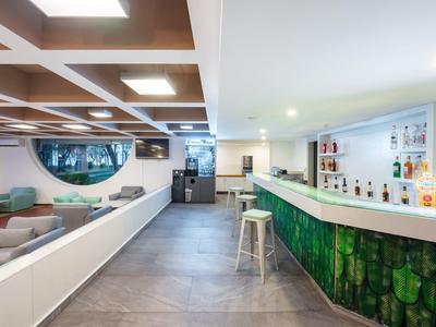 Moderner Hotelbarbereich mit weißem Tresen, Holzdecke und gemütlichen Sitzgelegenheiten.