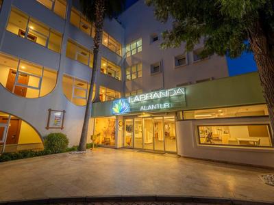 Beleuchteter Hoteleingang mit großen Fenstern und umliegenden Bäumen bei Nacht