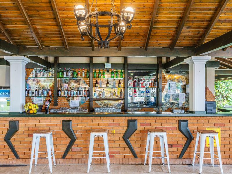 Helle Bar mit Holzdecke, Backsteinfront und weißen Barhockern unter einem Kronleuchter.