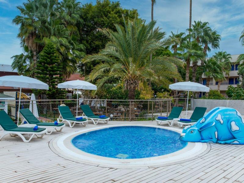 Kleiner Pool mit wasserrutsche und Liegestühlen auf einer Holzterrasse umgeben von Palmen.