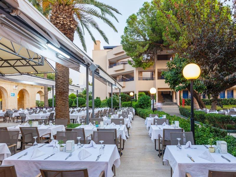 Außenrestaurant mit weiß gedeckten Tischen und Stühlen in einem Gartenbereich eines Hotels.