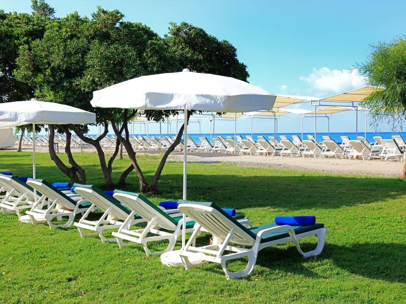 Weiße Liegestühle mit blauen Handtüchern unter Sonnenschirmen auf grünem Rasen vor einem Pool