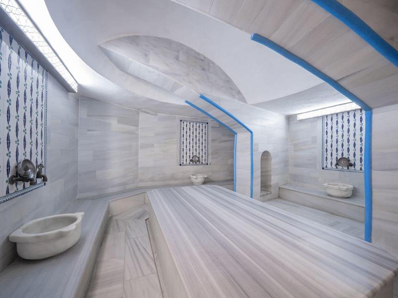 Heller, moderner Hammam mit Marmorwänden und Liegeflächen, zwei Waschbecken und blauen Akzenten.