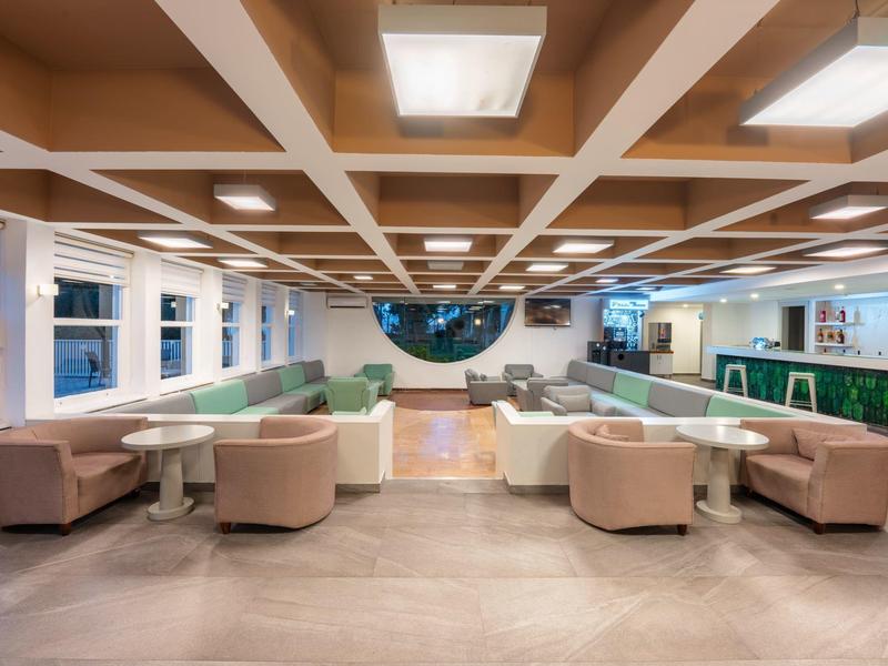 Helle, moderne Hotel-Lounge mit Sitzgruppen, großem Fenster und dekorativer Decke.
