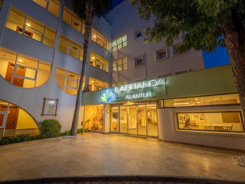 Beleuchteter Hoteleingang mit großen Fenstern und umliegenden Bäumen bei Nacht