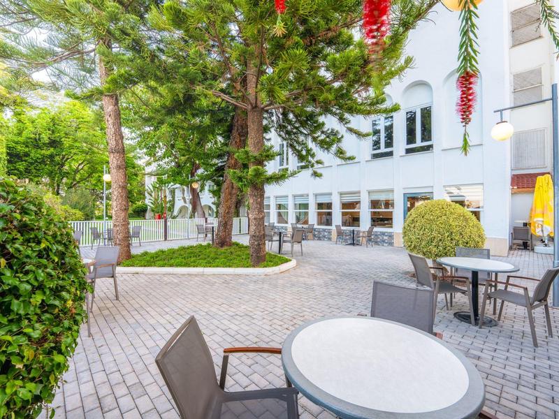 Außenbereich eines Hotels mit Tischen, Stühlen und grünen Pflanzen auf gepflastertem Boden