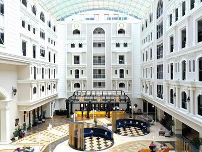 Heller, großer Innenhof mit weißer Fassade, Glasdach und Sitzbereichen auf Marmorfußboden.