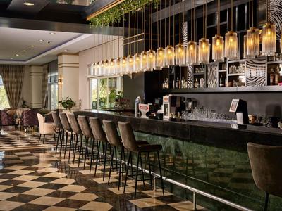 Moderner Barbereich mit Holzstühlen, schwarzen Tresen und Hängeleuchten in warmem Ambiente.